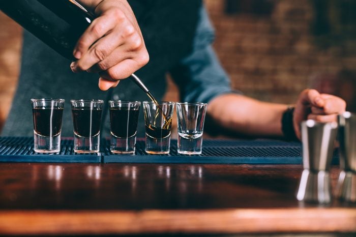 Bartender pouring strong alcoholic drink into small glasses on bar counter