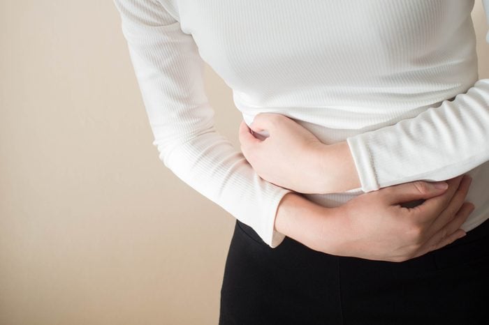 Young female suffering form stomach ache on gray background w/ copy space. Causes of abdominal pain include menstruation pain, gastritis, stomach ulcer, food poisoning, diarrhea or IBS. Close up.