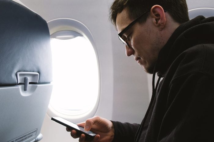 Man in glasses uses a smartphone on a plane, sitting at the window, 4k.