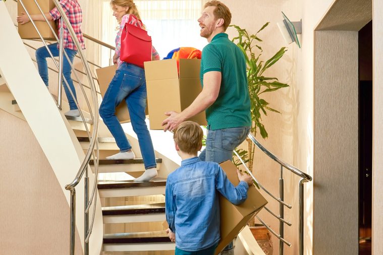 Family carrying boxes upstairs. Group of people indoors. Moving to a new place.