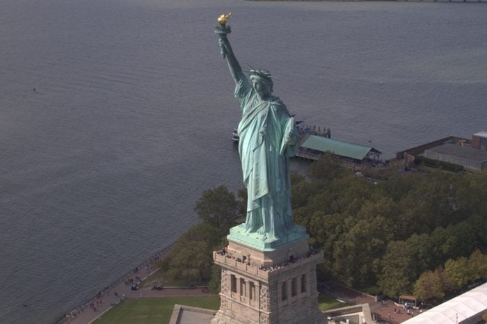 AERIAL, CLOSE UP, ESTABLISHING SHOT: Flying around Lady Liberty statue on island full of tourists in New York Hudson River. Famous Statue of Liberty standing proudly in New York