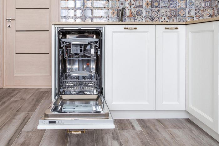 Build-in dishwasher with opened door in a white kitchen in neoclassical style with wooden front 