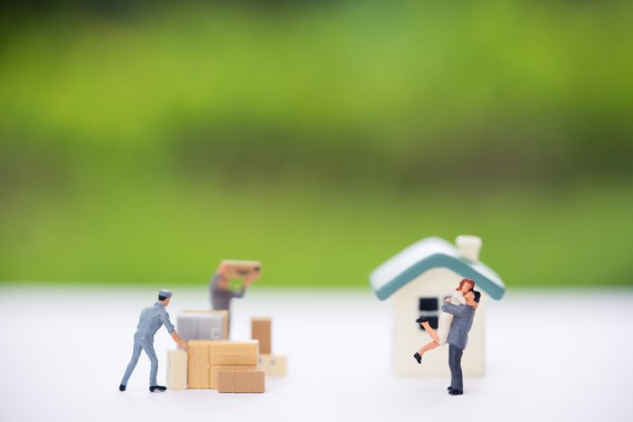 Miniature people, couple in front of new house and workers moving stuffs. Concept of moving house, relocation.
