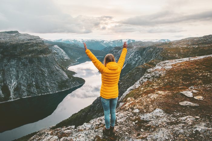 Happy woman raised hands on mountain summit traveling alone adventure lifestyle journey vacations aerial lake landscape success wellness emotions 