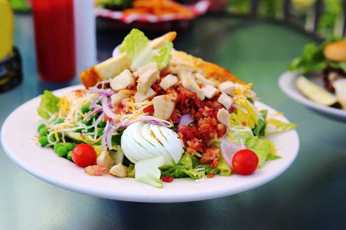 Crisp fresh lettuce with cherry tomatoes, bacon, and hardboiled egg adorn a chicken Cobb Salad