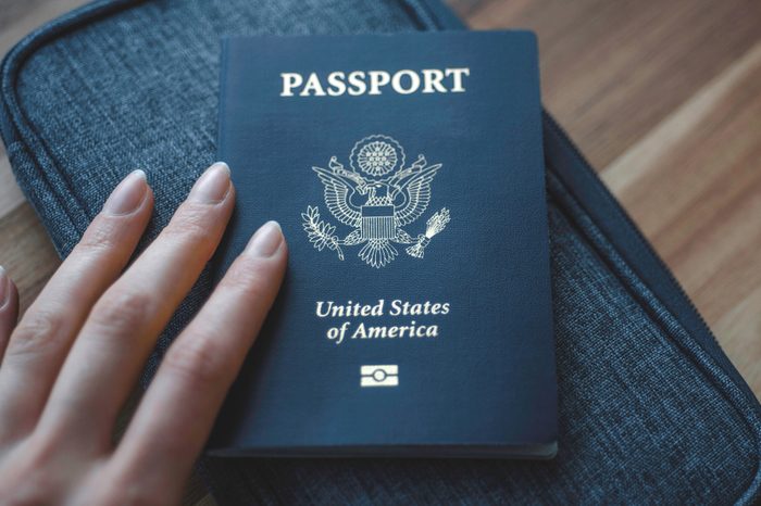 Woman's fingers holding Passport of USA (United States of America) on blue travel wallet and wooden background. 