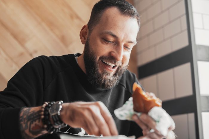 Young bearded man eating burger and smiling close up.