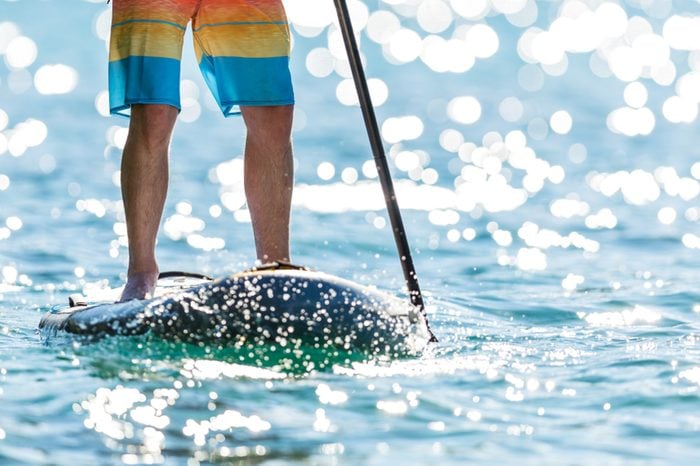 Detail of young man standing on paddleboard. Paddleboarding is the modern way of transportation and water activity sport.