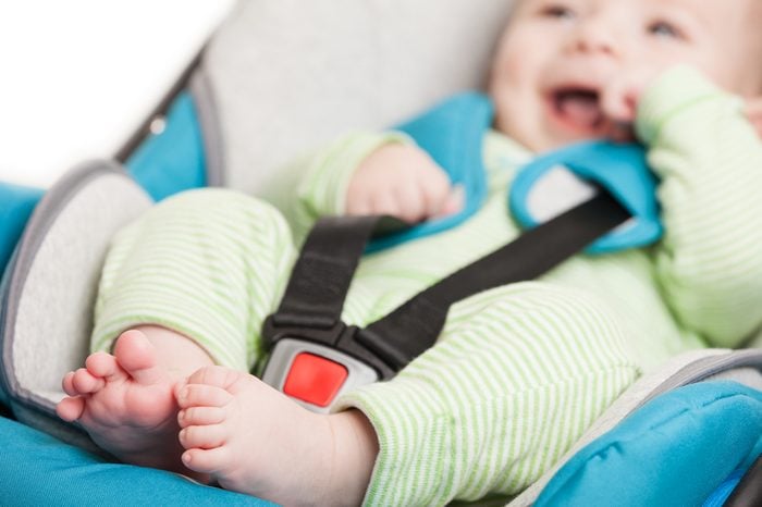 Little smiling baby child fastened with security belt in safety car seat