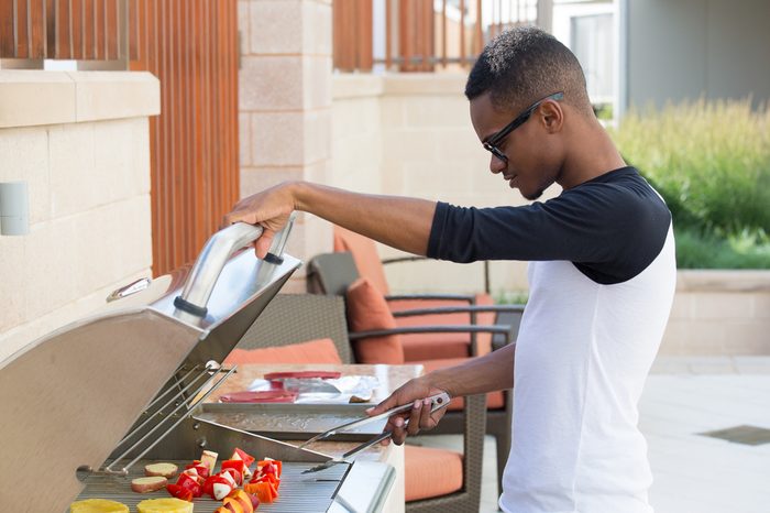 Closeup portrait, handsome young guy with big glasses barbecuing yummy food, isolated outside background