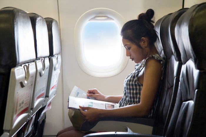 Young woman travels in a chair of the airplane. Passengers reads a magazine in the window of the aircraft. Enjoy - entertainment on board of flying air plane.