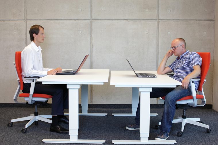 man working in correct sitting posture in office watching his colleague sitting in bad position at workstation
