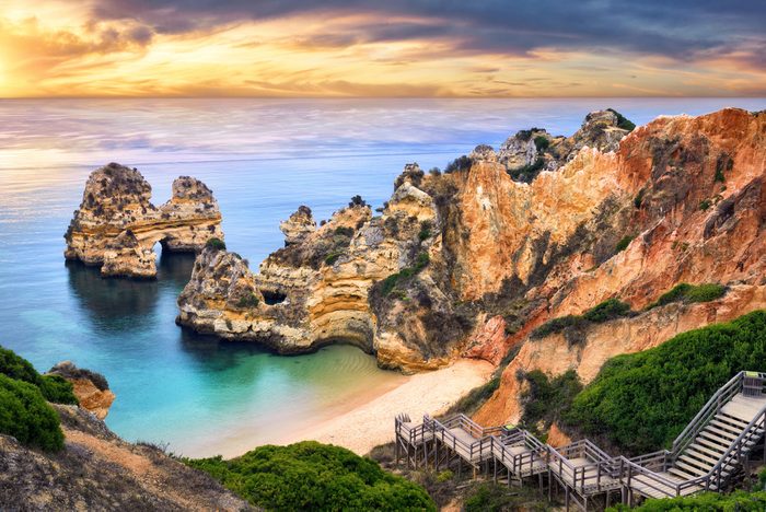 The beautiful Camilo Beach in Lagos, Portugal, with its magnificent cliffs and the blue ocean colorfully lit at sunrise