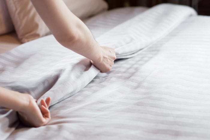Close up woman hand set up white bed sheet in hotel room