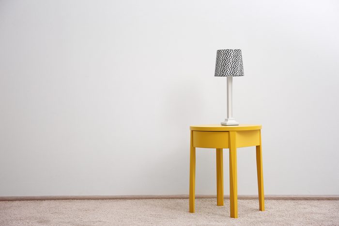 Yellow bedside table with lamp on white wall background