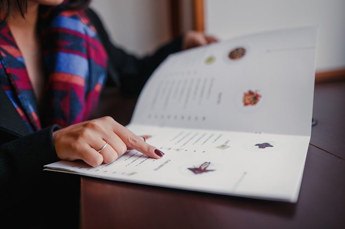 close up of woman finger with menu choosing dishes at restaurant