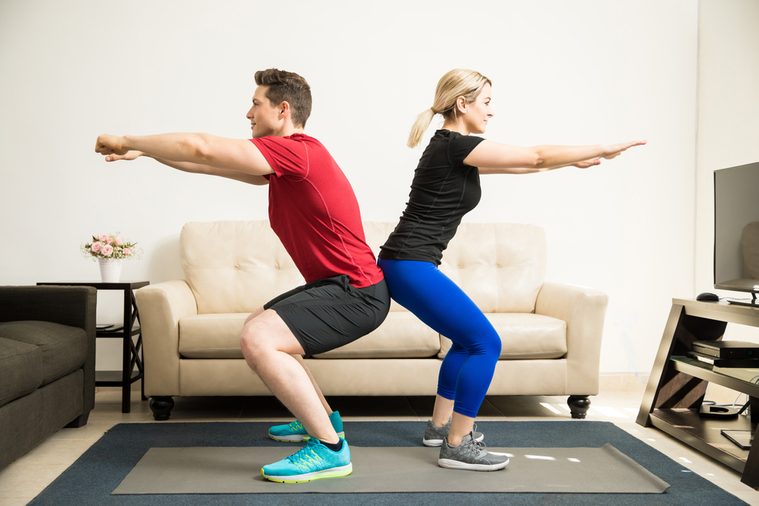 Profile view of a young Latin couple exercising and doing some squats together at home