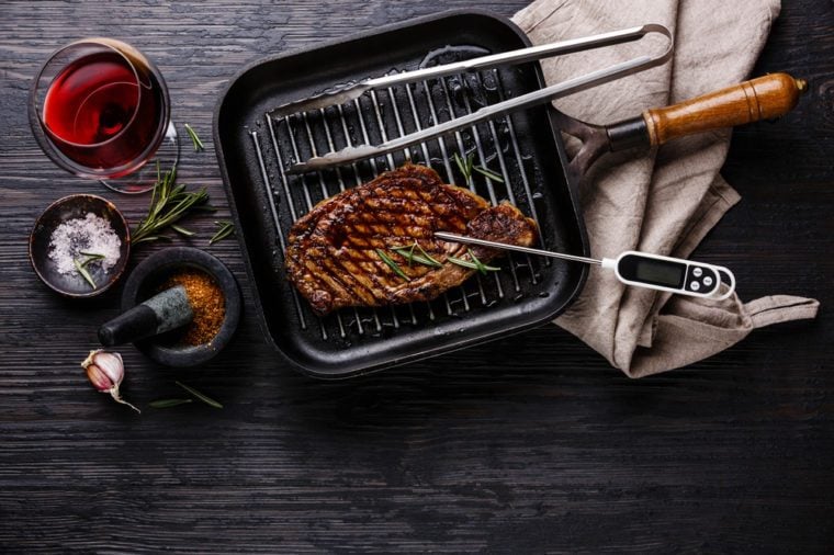 Grilled Steak Striploin on pan and meat thermometer on black burned wooden background copy space