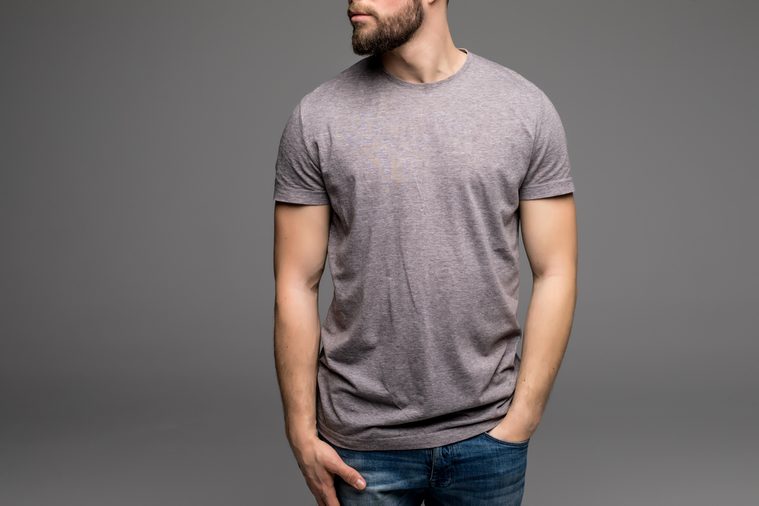 A man in a grey t-shirt and denims holds his hands in pockets. Isolated on grey