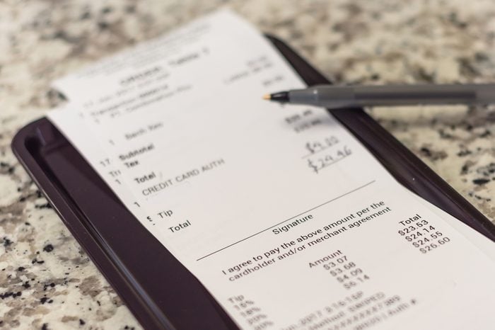 Soft focus, shallow DOF a receipt with hand written total amount and tipping from Vietnamese restaurant. Paper invoice with suggested gratuities/tips on plastic tray, open pen on top of marble table.