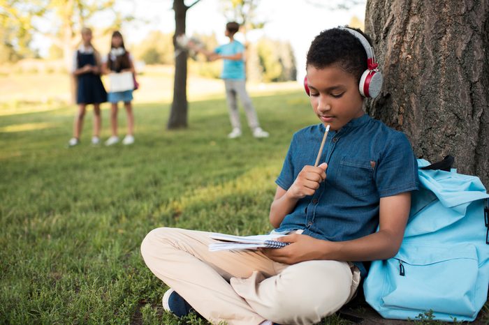 pensive african american boy in headphones taking notes and studying in park