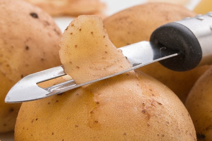 Potatoes, with a vegetable peeler on a white background, close up 