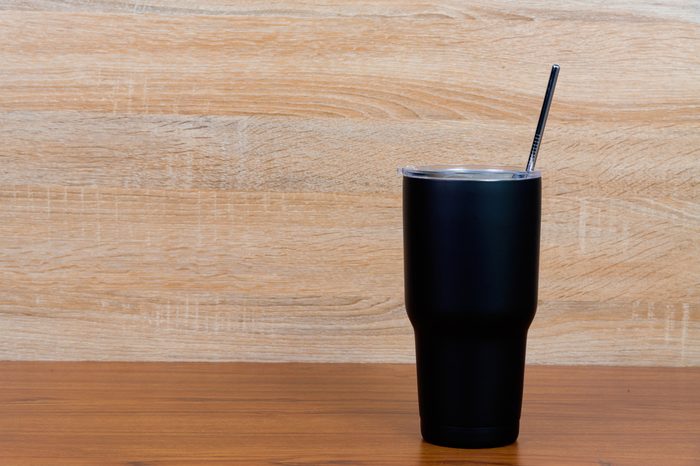 Black colour stainless steel tumbler or cold storage cup with water straw and cap on wooden background.