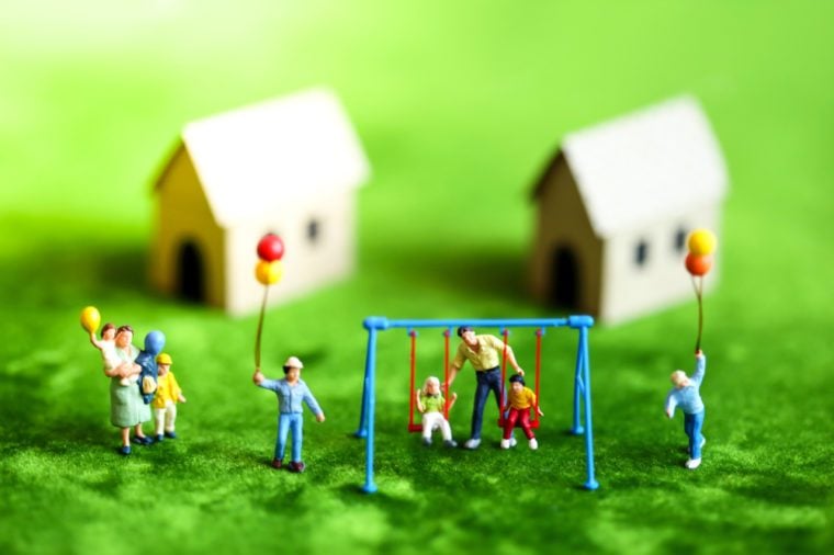 Miniature people with happy family holding balloons in front of wooden house on green background as property or mortgage concept.