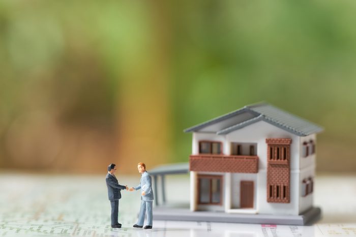 Miniature 2 people businessmen Shake hands with A model house model .as background business concept and real estate concept with copy space.