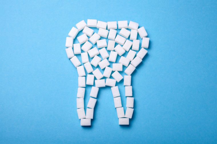 Sugar destroys the tooth enamel and leads to tooth decay. Sugar cubes are laid out in the form of a tooth on a blue background.