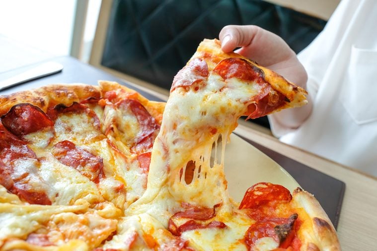 Delicious fresh hot talian pizza slice with melting cheese on wooden table.