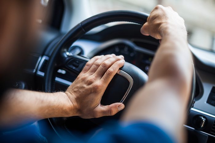Close up shot of a man's hands holding a car's steering wheel and honking the horn.
