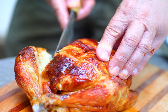 A man steadies a chicken with one hand as he cuts with the other