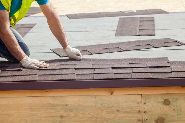 Roofer builder worker installing roof shingles 