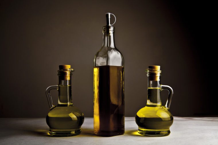 Backdrop of three olive oil glass transparent bottle with cork stand on white table on kitchen space room, on dark black background Empty space for inscription 
