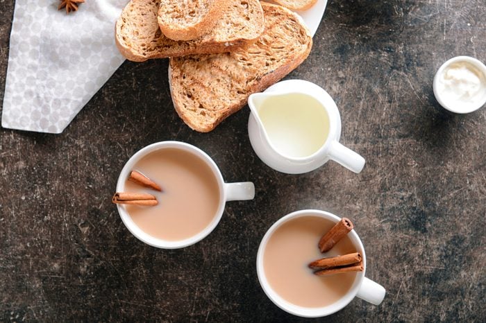 Cup of aromatic tea with cinnamon, milk and fresh bread on table