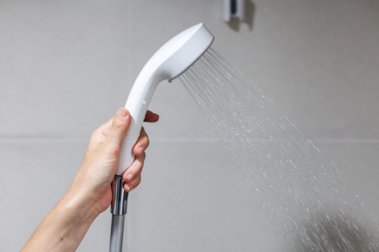 Housewife holds in her hand cleen and closed off rain shower head in the bathroom.