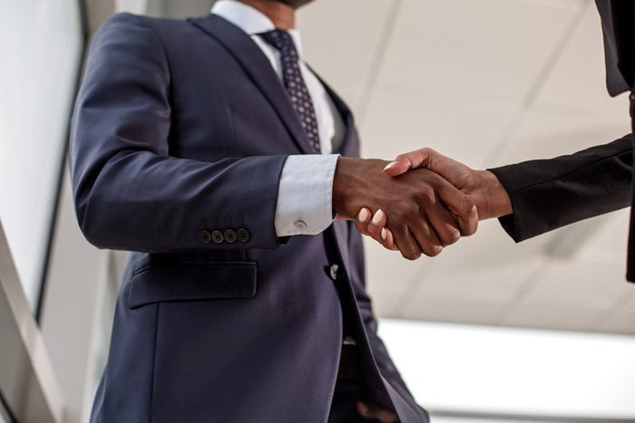 Good work. Low angle close-up of strong handshake of intelligent businesspeople. Elegant man and woman are standing in office wearing formal clothes