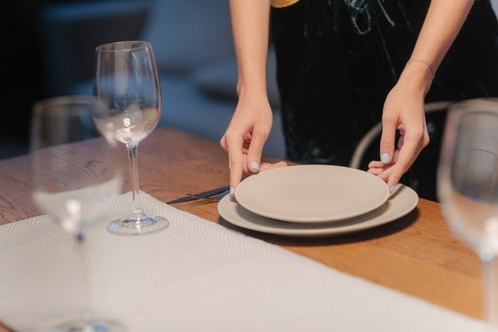 Young woman setting up table for dinner party at home.