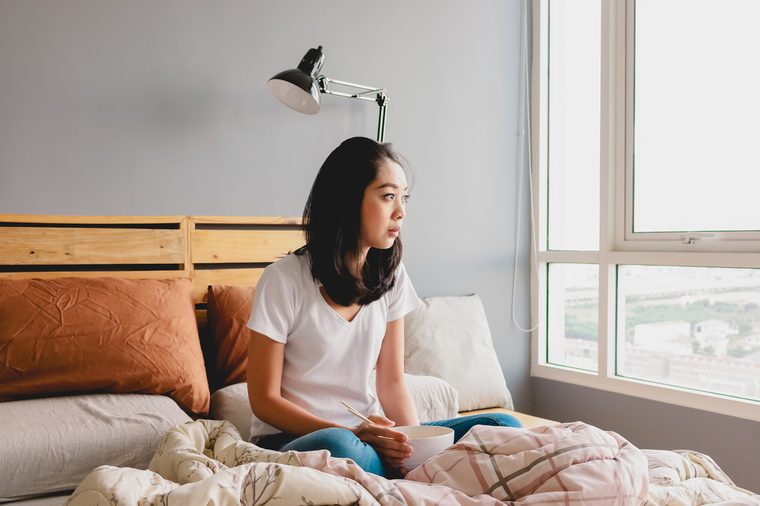 Lonely Asian woman is eating alone on bed in bright morning.