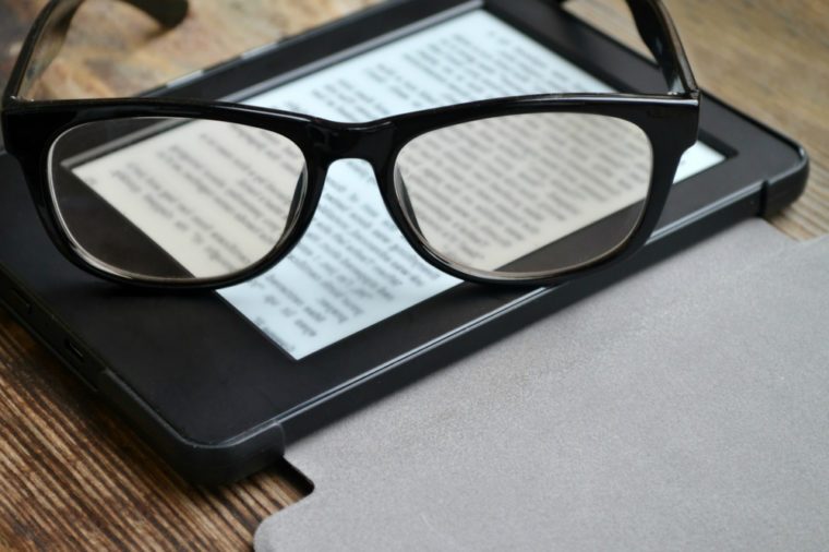 Black ereader with retro glasses on wooden table