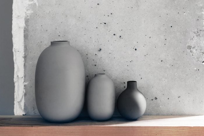 Home interior decor in scandinavian minimalistic style: ceramic vases on the wooden shelf over concrete wall. Living room decoration in gray colors.