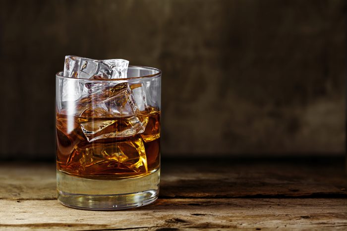 glass of scotch whiskey with ice cubes on a rustic wooden table, copy space in the brown background