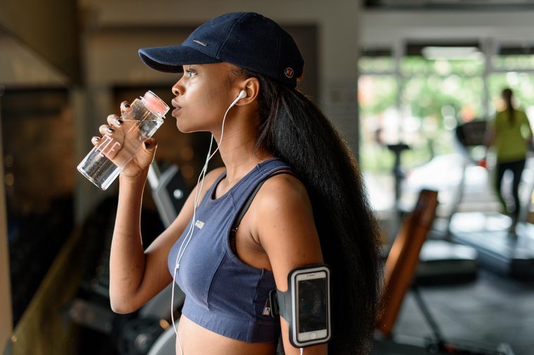 Side view of gorgeous black female athlete drinking water from bottle in the gym