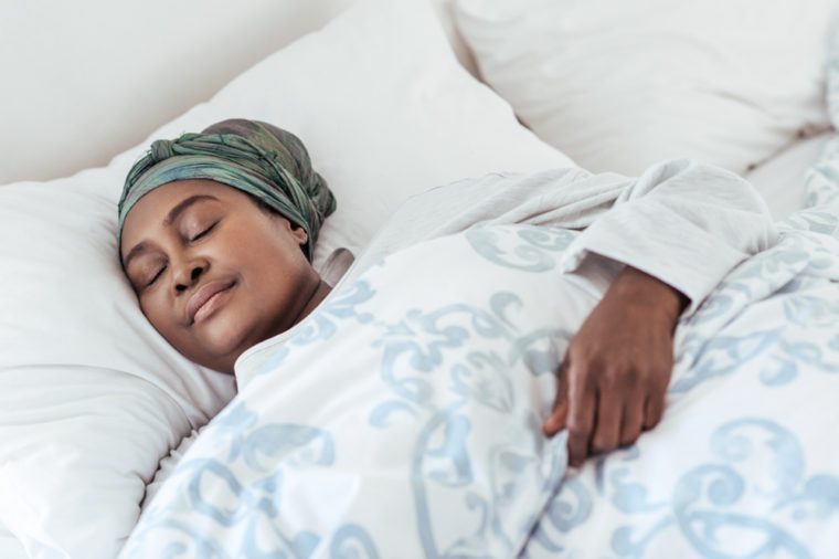 Young African woman wearing a headscarf fast asleep under the covers of her bed at home in the early morning