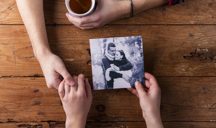 Unrecognizable man holding womans hand. Looking at their photo. Couple 