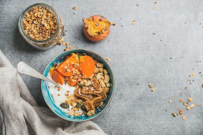 Healthy breakfast concept. Oatmeal, quinoa granola with yogurt, dried fruit, seeds, honey, persimmon in bowl over grey concrete background, top view, copy space. Allergy-friendly, gluten free concept