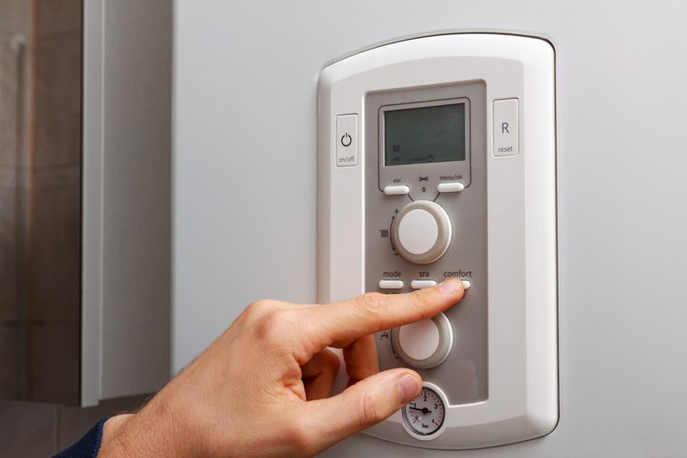 Men hand setting comfort temperature button on control panel of central heating or DHW at combi boiler in restroom.