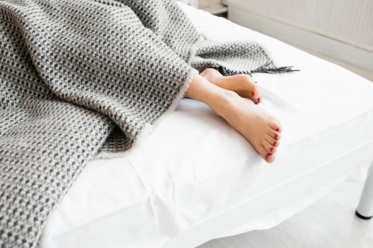 Woman feet under gray blanket sideview. Beautiful young woman feet with red pedicure on the bed. Sleeping woman legs under the gray blanket