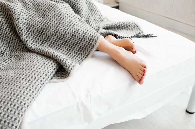 Woman feet under gray blanket sideview. Beautiful young woman feet with red pedicure on the bed. Sleeping woman legs under the gray blanket